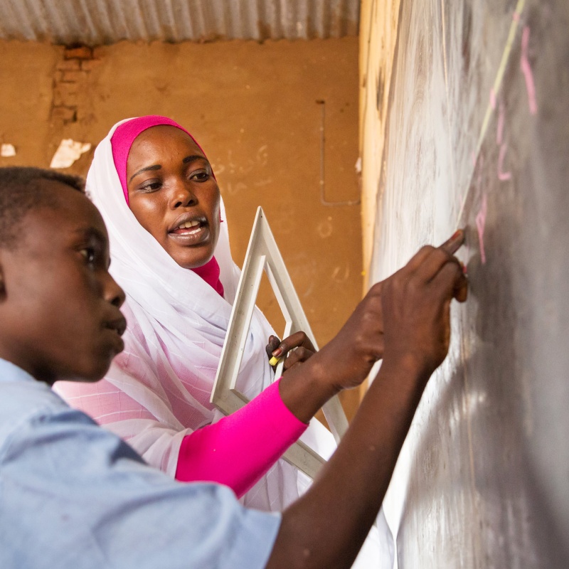Teacher with student at Umdebekrat Basic School for Boys, recipients of a GPE school grant and textbooks; Nyala South Locality, South Darfur, Sudan. Credit: GPE/ Kelley Lynch